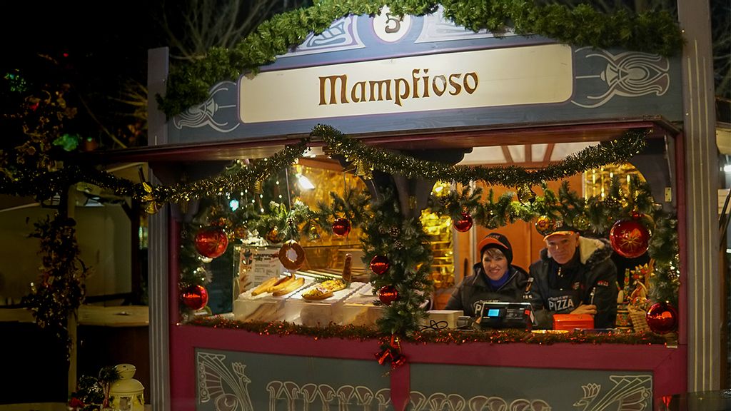 Weihnachtsmarkt-Stand bei Nacht mit Verkäufer*innen hinter dem Tresen