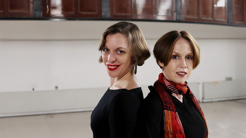 Zwei Schauspielerinnen stehen Rücken an Rücken und lächeln die Kamera
