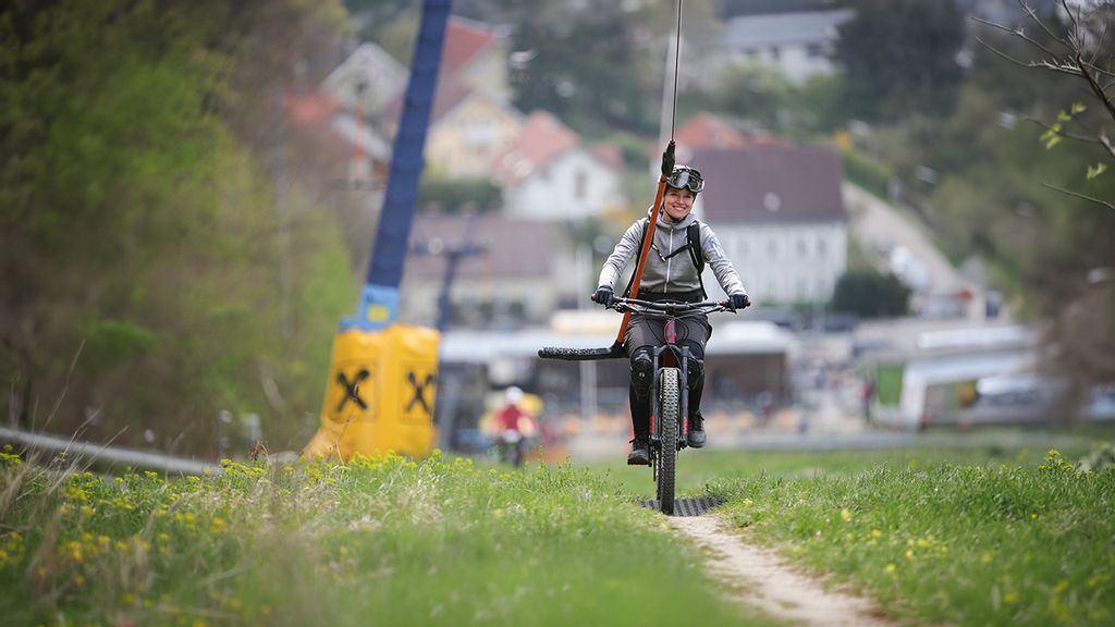 Eine Frau fährt mit einem Bike am Lift den Berg hoch