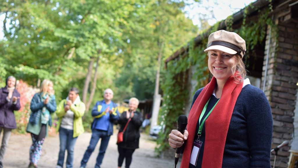 Workshopleiterin mit rotem Schal und einer Kappe sowie Teilnehmer im Hintergrund