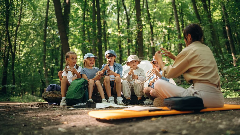 Gruppe an Kindern sitzen mit einer Betreuerin zusammen im Wald