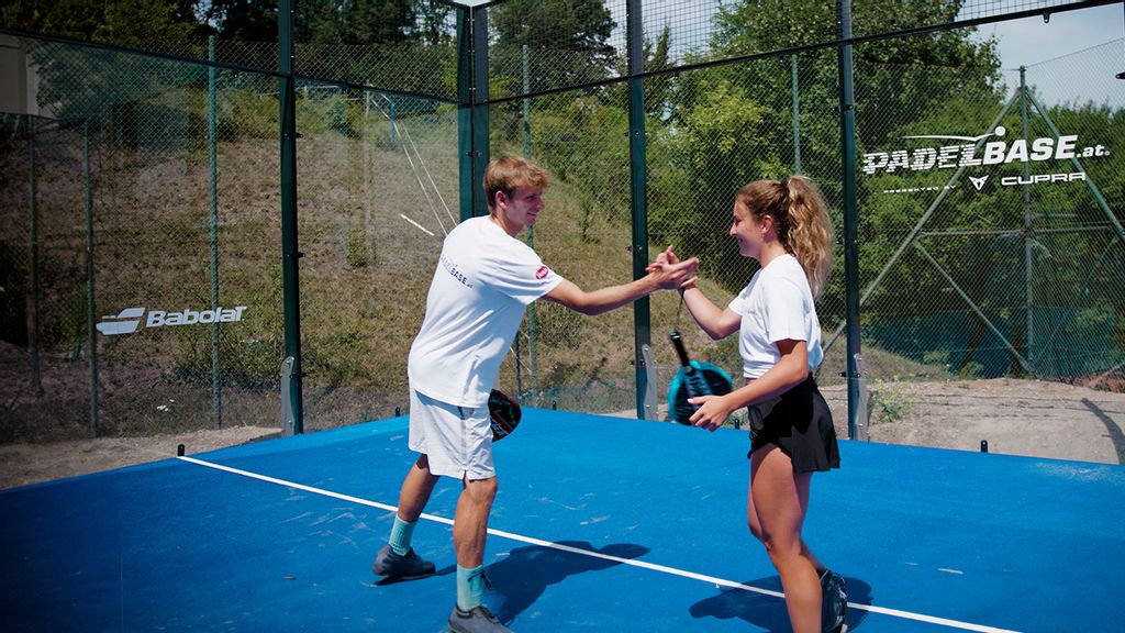 Ein Mann und eine Frau stehen am Padelplatz und klatschen sich gegenseitig in die Hände 