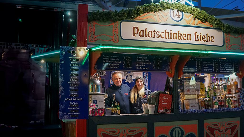 Weihnachtsmarkt-Stand bei Nacht mit Verkäufer*innen hinter dem Tresen