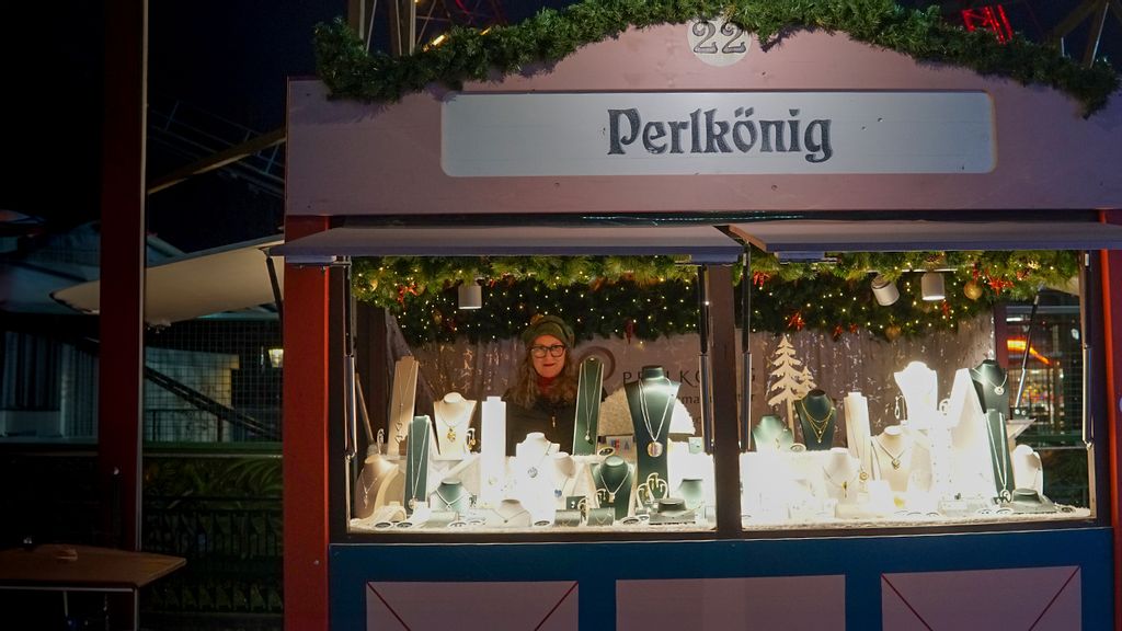 Weihnachtsmarkt-Stand bei Nacht mit Verkäuferin hinter dem Tresen.