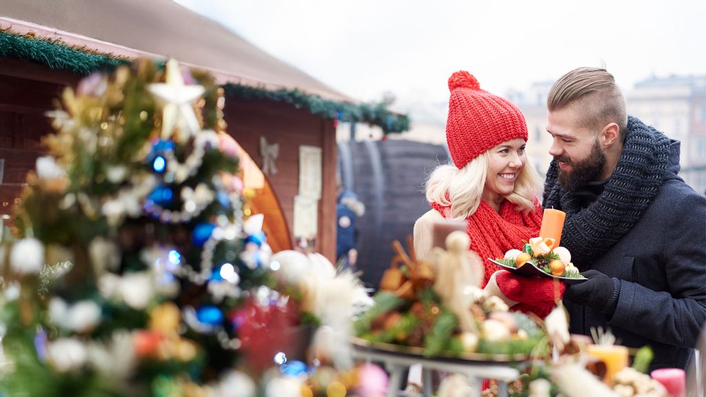 Eine Frau und ein Mann schauen sich auf einem Adventmarkt eine Weihnachtskerze an