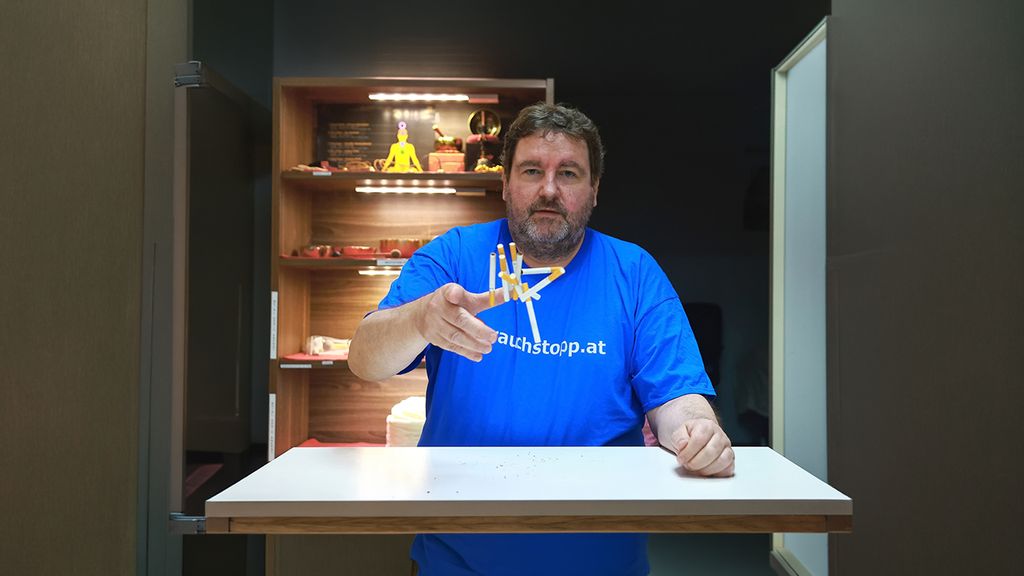Mann in blauem Shirt sitzt in einem Behandlungsraum und wirft mit Zigaretten