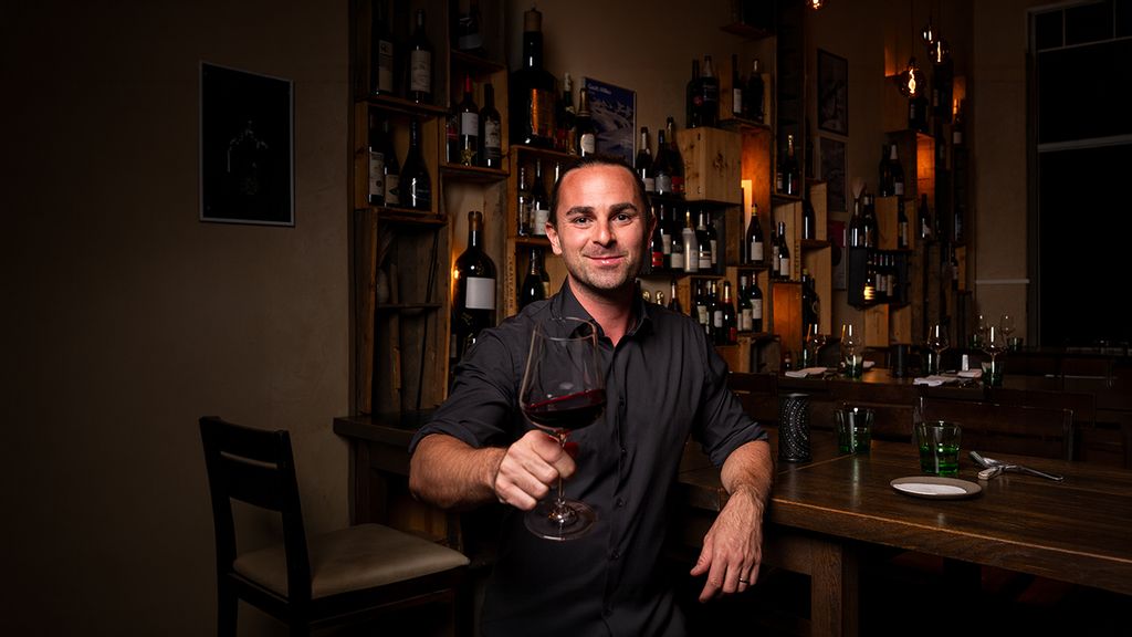 Person sitzt an einer stilvollen Bar mit einem Weinglas in der Hand
