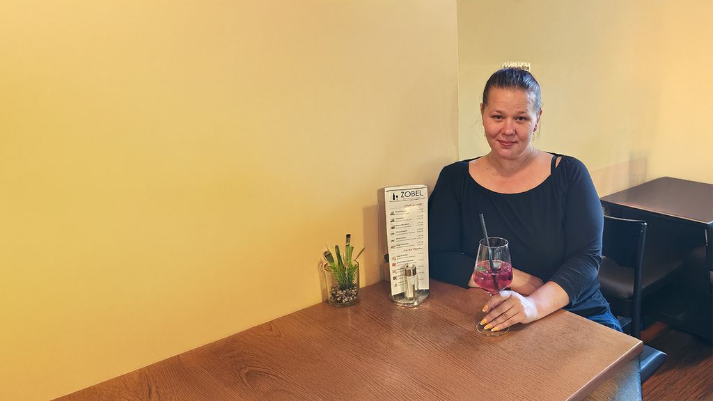 © Restaurant Zobel Frau mit einem Getränk in der Hand sitzend an einem Holztisch