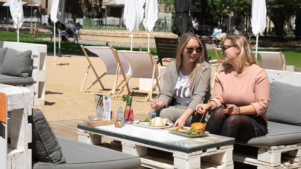 Zwei Frauen sitzen auf einem Sofa in der Sonne und haben Speisen und Getränke vor sich