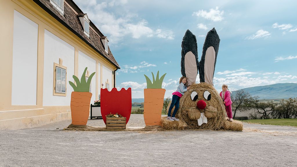 Zwei Kinder spielen auf einem Osterhasen-Strohballen vor einem Gebäude vom Schloss Hof