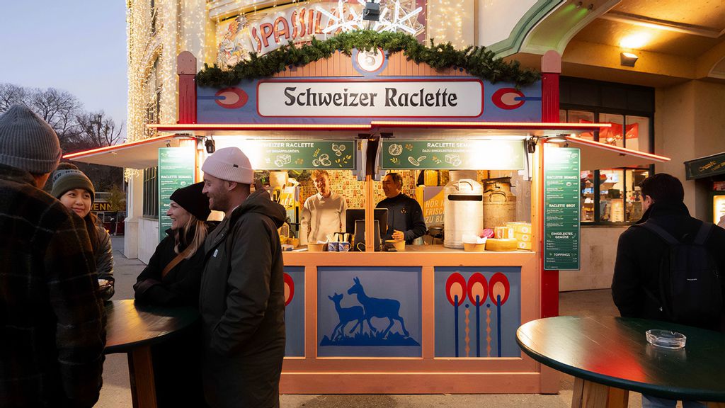 Zwei Mitarbeiter und mehrere Personen am Wintermarkt vor bzw. in einer Hütte.