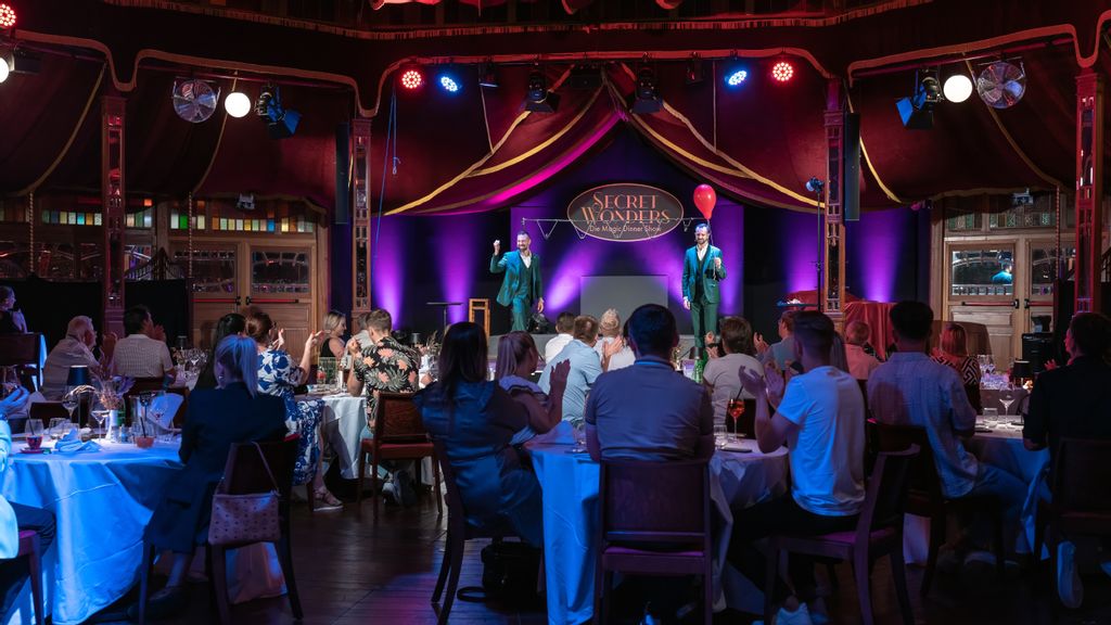 Applaudierende Gäste während einer Dinner Show, auf der zwei Zauberer auf der Bühne auftreten