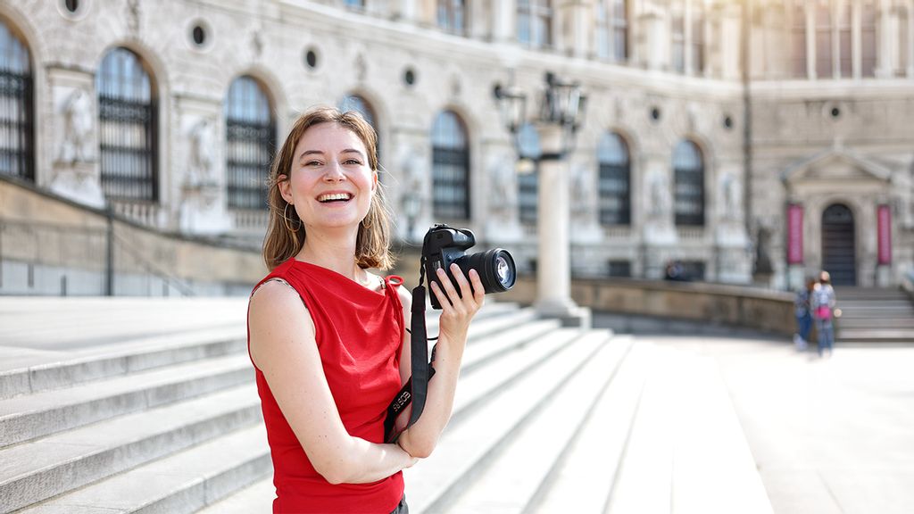 Fotografin steht in der Innenstadt auf Stiegen und hält eine Kamera in der Hand