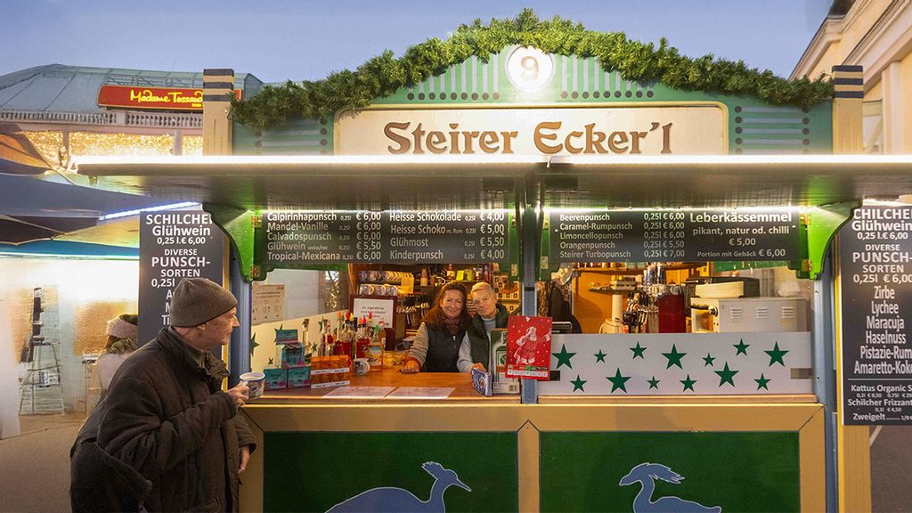 Weihnachtsmarkt-Hütte mit zwei Verkäuferinnen und einem Mann, der einen Punsch hält.