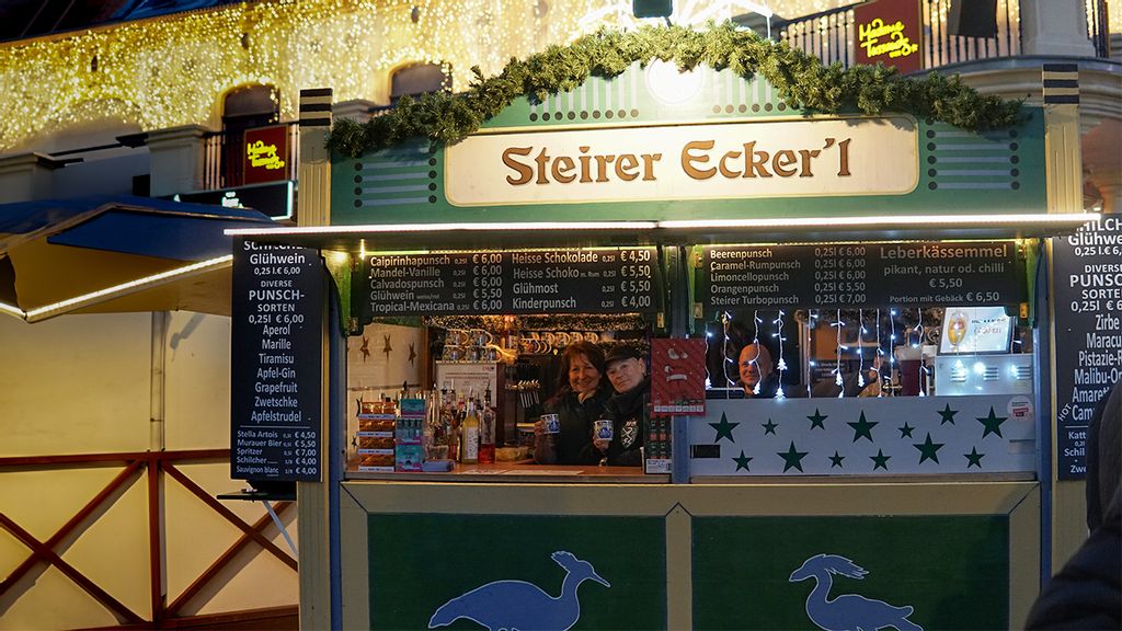 Weihnachtsmarkt-Hütte mit zwei Verkäuferinnen und einem Mann, der einen Punsch hält.