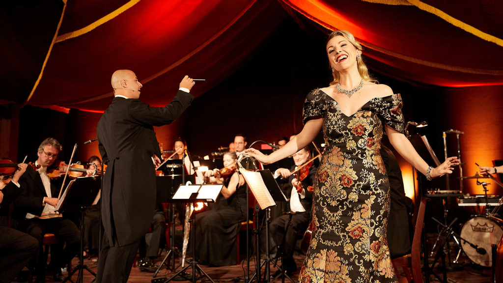 eine Frau in buntem Kleid singt auf einer Bühne vor einem Orchester