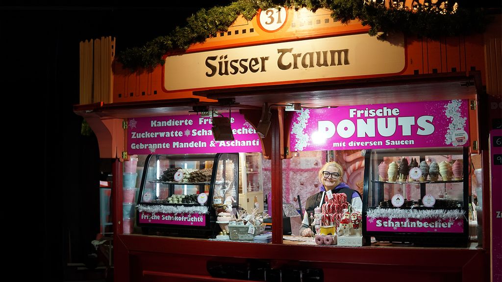 Weihnachtsmarkt-Stand bei Nacht mit Verkäuferin hinter dem Tresen.