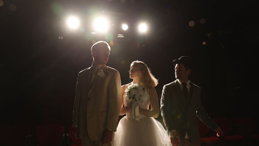 Zwei Männer und eine Frau mit Blumenstrauss in der Hand auf Bühne