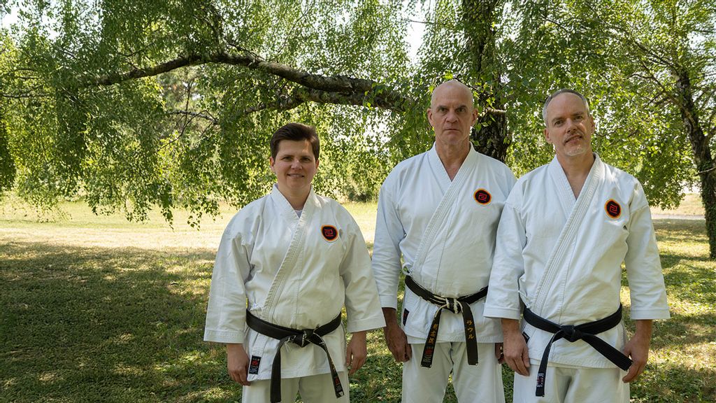 Zwei Männer und eine Frau in der traditioneller Karate Kleidung stehen im Freien auf einer Wiese