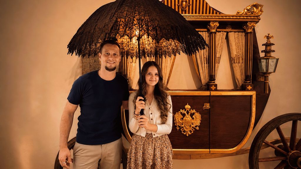 Ein Mann und eine Frau in einem Museum vor einer historischen Kutsche