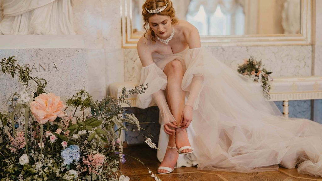 Eine Frau im Hochzeitskleid zieht im sitzen ihre Schuhe an. Neben ihr ist ein Blumengesteck.