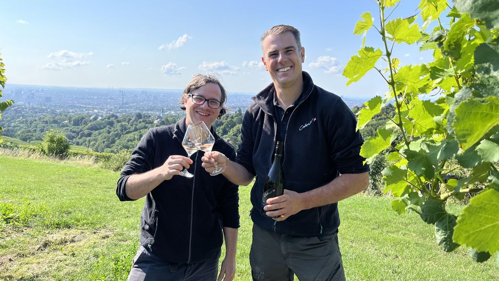 Zwei Personen bei einem Weingut stoßen mit einem Weinglas an