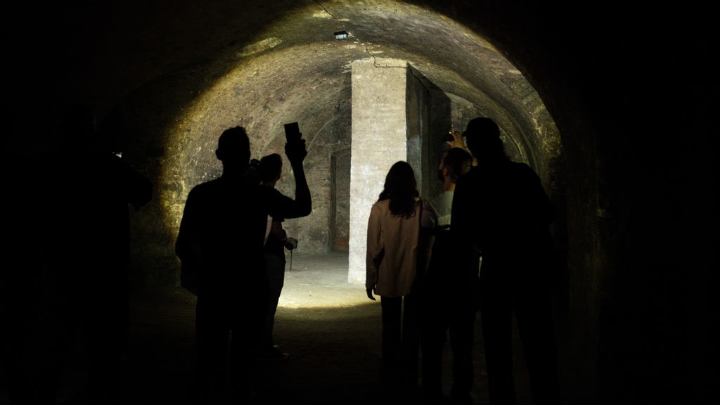 Besucher*innen gehen mit Taschenlampen durch einen Kanal