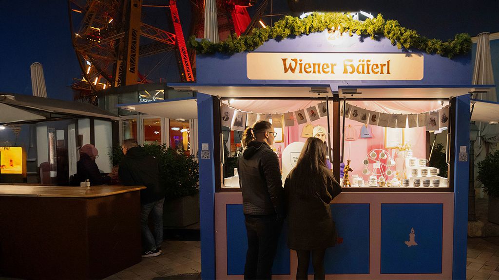 Ein Mitarbeiter in der Hütte und zwei Personen vor der Hütte am Wintermarkt