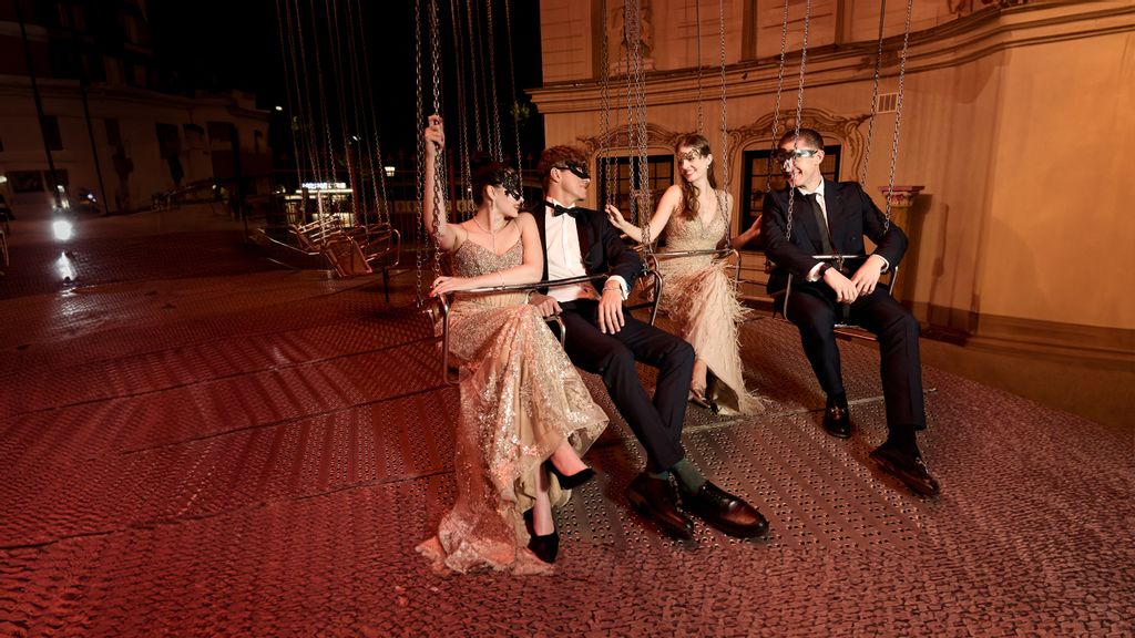 Vier Personen in festlicher Kleidung und Maske sitzend in einer Karussell Schaukel 