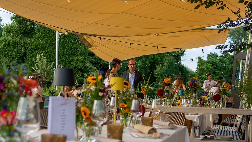 Personen stehen mittig in einem Sommergarten eines Restaurants