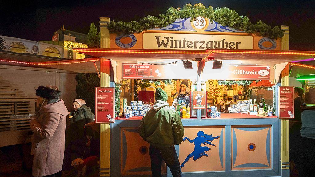 Eine Mitarbeiterin in der Hütte und mehrere Personen vor bzw. neben der Hütte am Wintermarkt