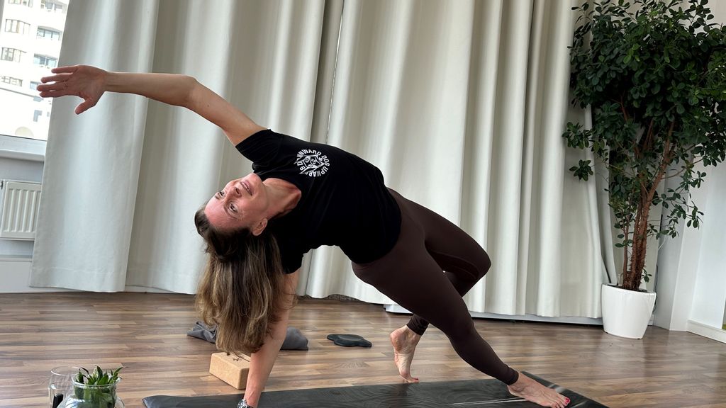 Frau in Trainingsgewand auf der Yoga-Matte beim Dehnen