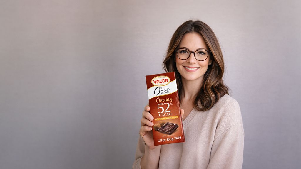 Lächelnde Person mit Brille hält eine VALOR Zero Schokoladenpackung vor grauem Hintergrund.