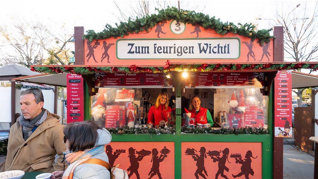 Zwei Mitarbeiterinnen und mehrere Personen am Wintermarkt vor bzw. in einer Hütte