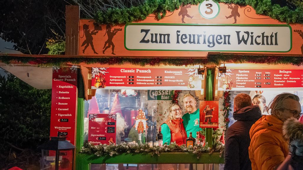 Zwei Mitarbeiterinnen und mehrere Personen am Wintermarkt vor bzw. in einer Hütte