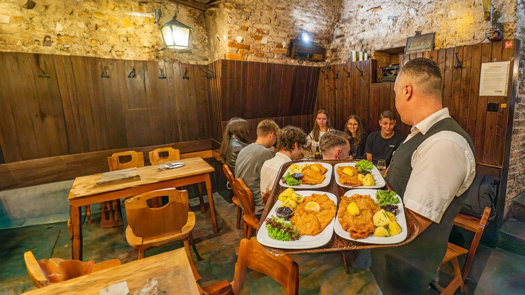 Gruppe von jungen Personen bekommt Wiener Schnitzel von einem Kellner serviert