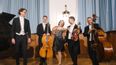 Fünf Musiker*innen mit Streichinstrumenten und Klavier auf einer Bühne