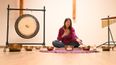 Eine Frau sitzt auf einer Yoga-Matte bei einer Klangschalen-Therapie