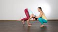 Zwei Frauen beim Yoga, wobei eine der anderen bei der Übung hilft