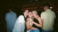 Drei junge Frauen umarmend und lächelnd in einer Bar