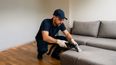 Ein Mann von einer Polsterreinigungsfirma reinigt ein Sofa in einer Wohnung