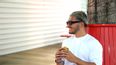 Ein Mann steht mit Sonnenbrille mit einem Burger in der Hand im freien und lächelt