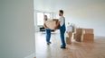 Zwei Möbelpacker tragen gemeinsam einen Umzugskarton in einer Wohnung