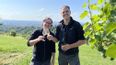 Zwei Personen bei einem Weingut stoßen mit einem Weinglas an