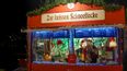 Weihnachtsmarkt-Stand „Zur heißen Schneeflocke“ bei Nacht mit Verkäufer hinter dem Tresen.