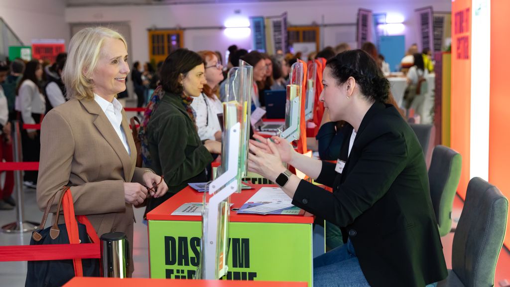 Eine Frau steht an einem Tisch und lässt sich von einer anderen Frau beraten