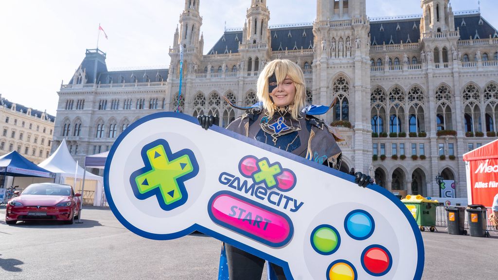 Eine verkleidete Person vor dem Wiener Rathaus mit einem übergroßen Controller in der Hand