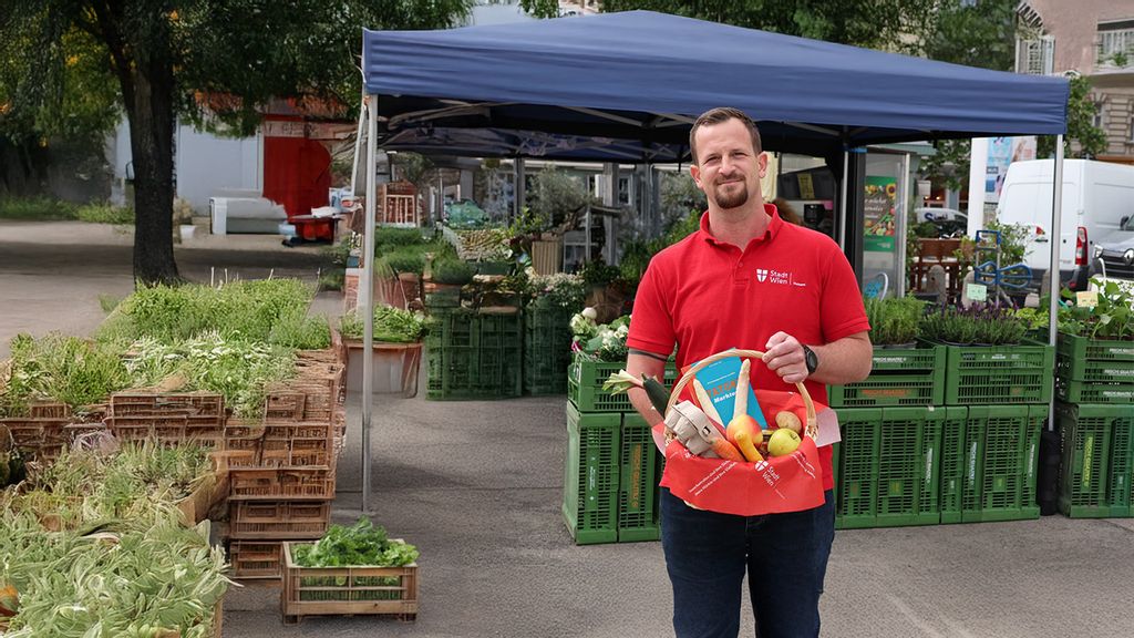 Ein Mann steht vor einem Marktstand und hält einen Korb mit Obst und Gemüse 