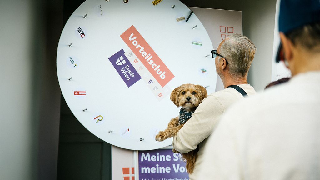 Eine Besucher mit Hund bei einem Vorteilsclub-Stand am #wienliebe Festival der am Glücksrad dreht