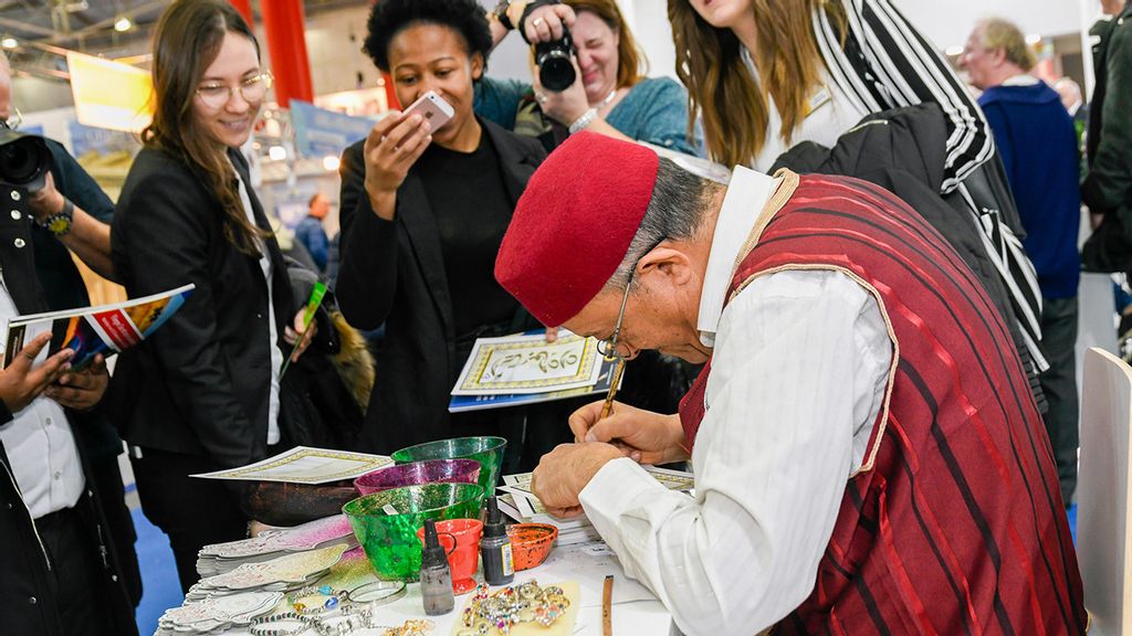 Besucher der Ferien-Messe betrachten einen Aussteller beim Herstellen von Schmuck